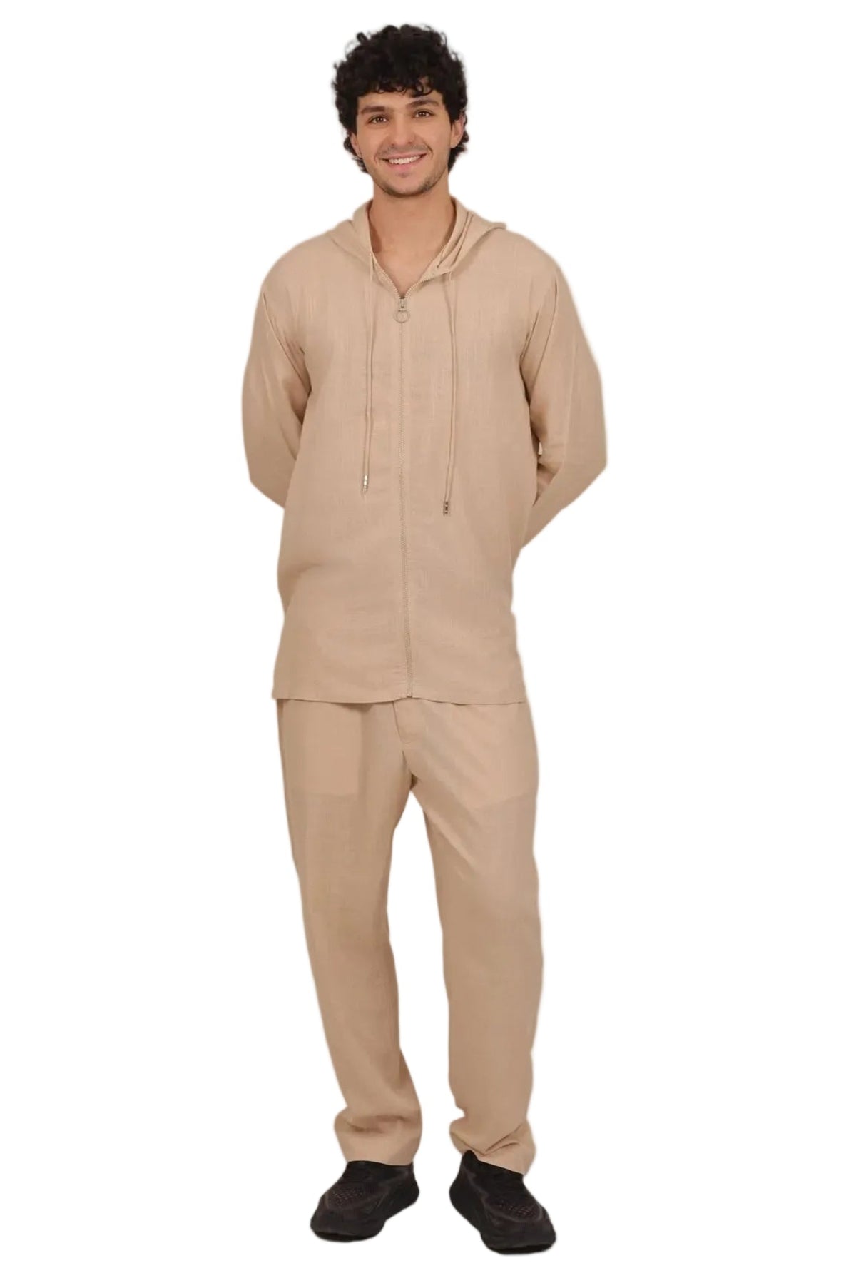 A man modeling a matching beige lounge set consisting of a zip-up hooded sweatshirt and sweatpants, paired with black shoes, against a plain white background.