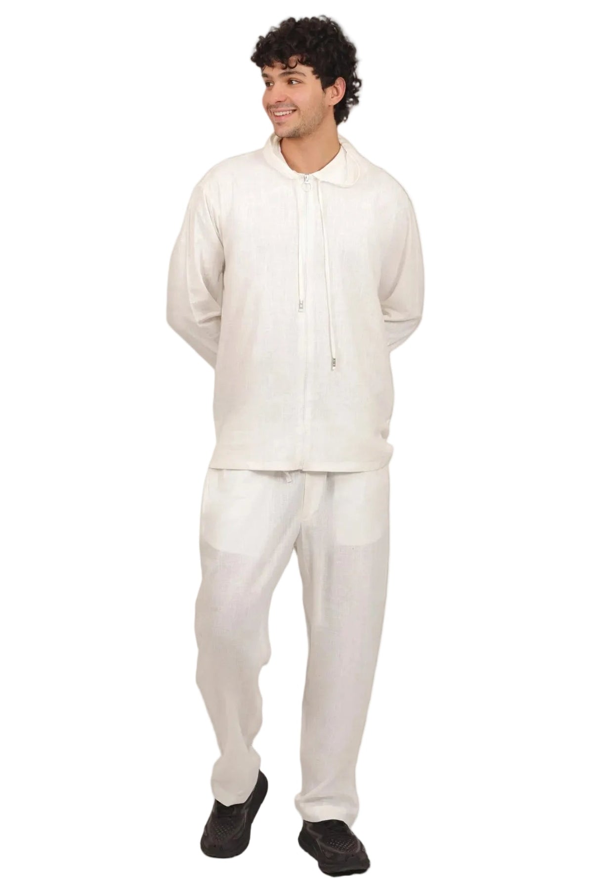 A man modeling a white two-piece linen loungewear set, consisting of a long-sleeve drawstring shirt and matching relaxed pants, against a solid white background.
