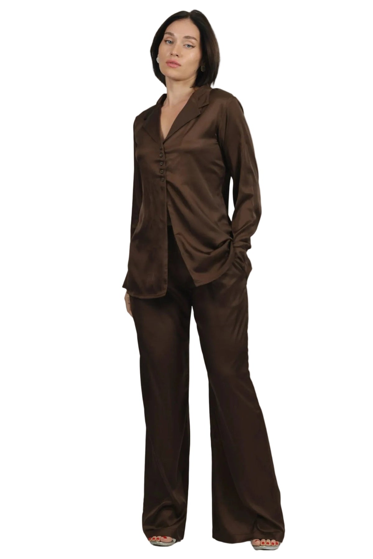 A woman modeling a matching brown satin pajama set consisting of a long-sleeve button-front top and wide-leg pants, photographed against a solid white background.
