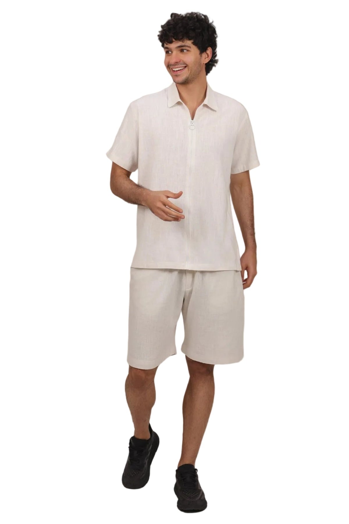 A man modeling a matching light beige short-sleeve button-up shirt and shorts set, paired with black sneakers, against a solid white background.