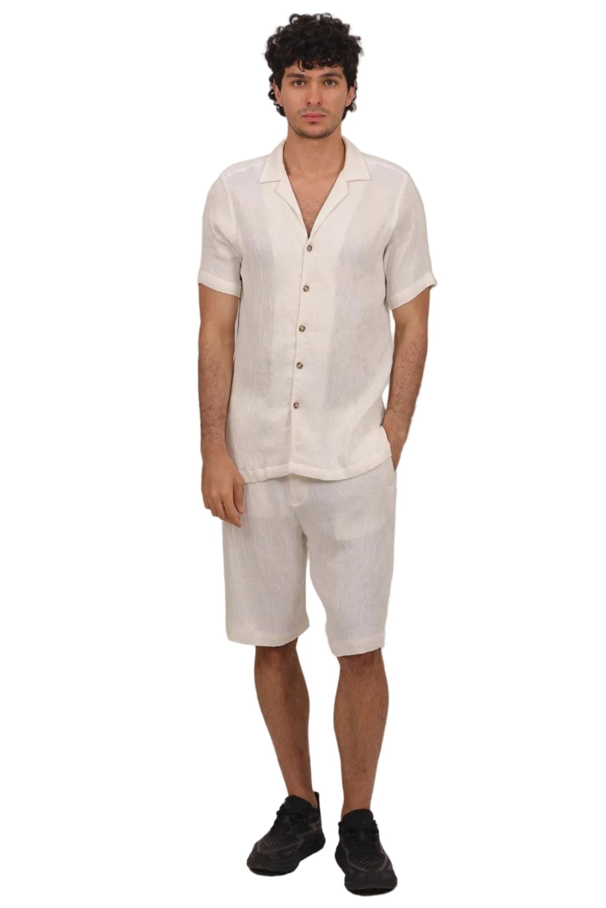 A man modeling a matching light beige linen short-sleeve button-up shirt and shorts set, paired with black sneakers, against a solid white background.