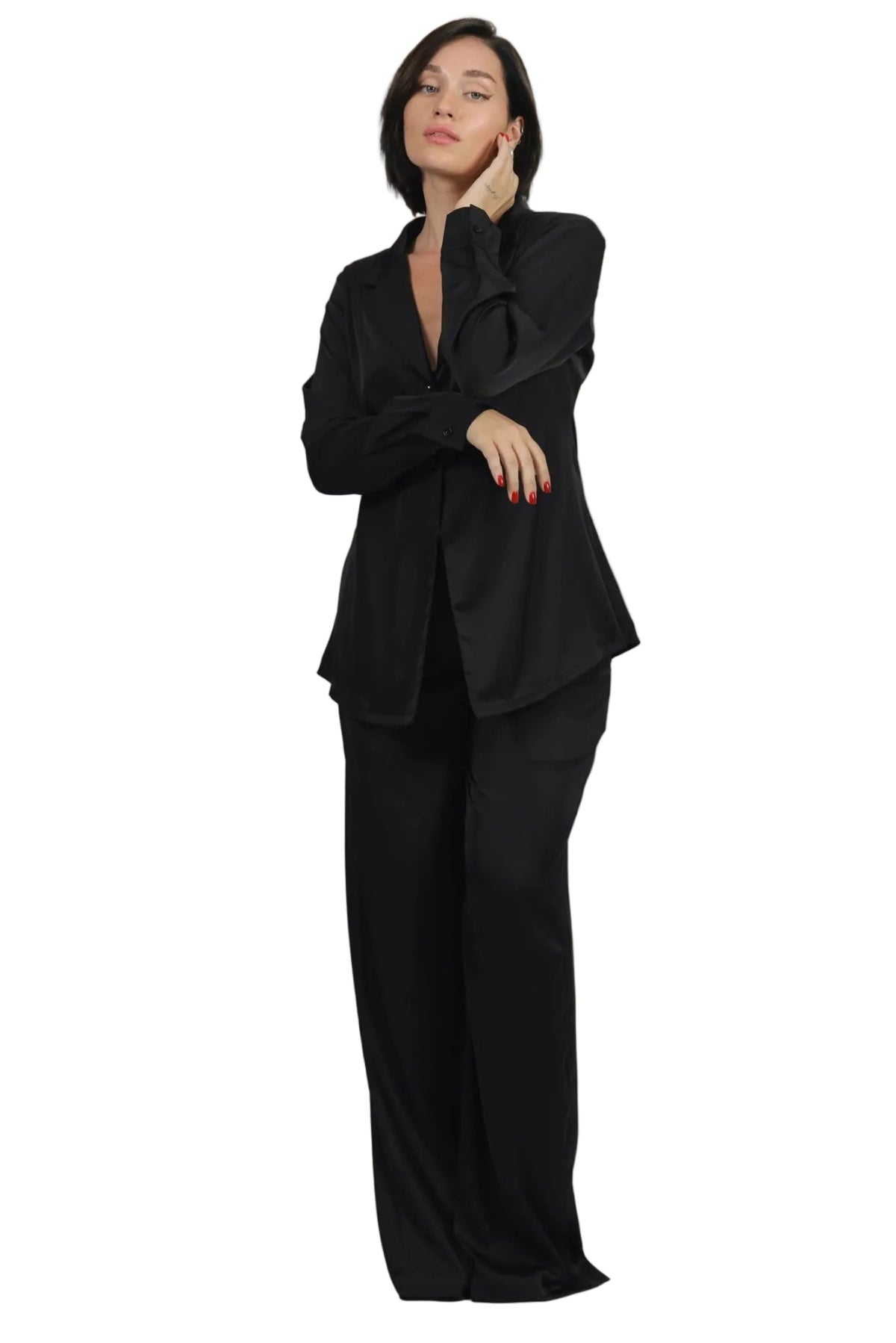 A woman modeling a black satin-like two-piece suit with a ruffled collar blazer and wide-leg trousers against a plain white background.