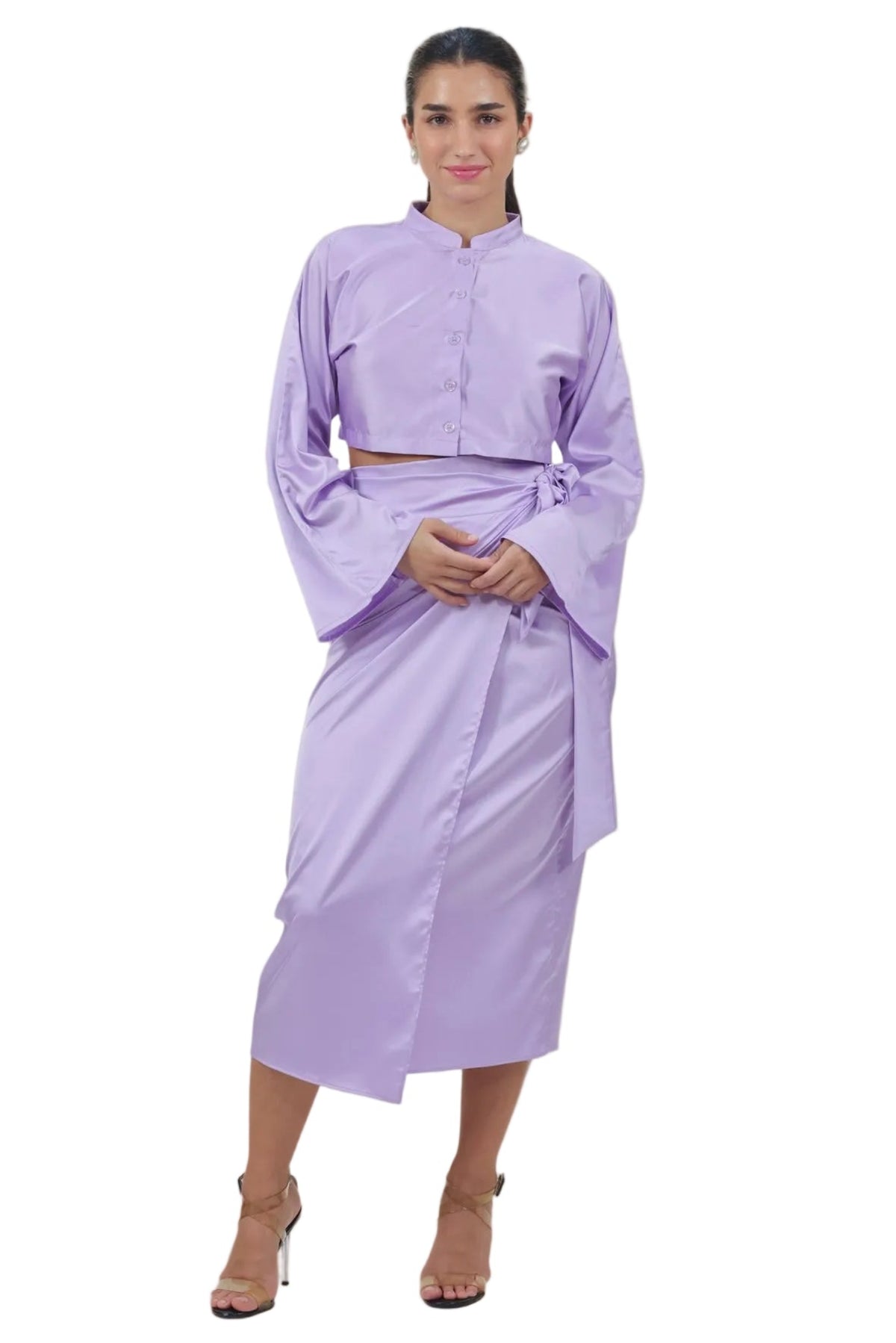 A woman modeling a lavender two-piece outfit consisting of a long-sleeve cropped top with wide sleeves and a matching midi skirt, set against a plain white background.