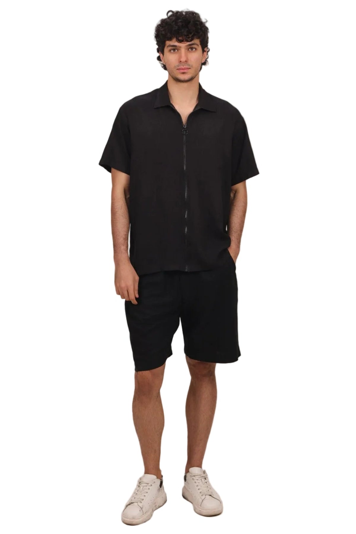 A man modeling a black short-sleeve button-up shirt and matching black shorts, paired with off-white sneakers, against a solid white background.