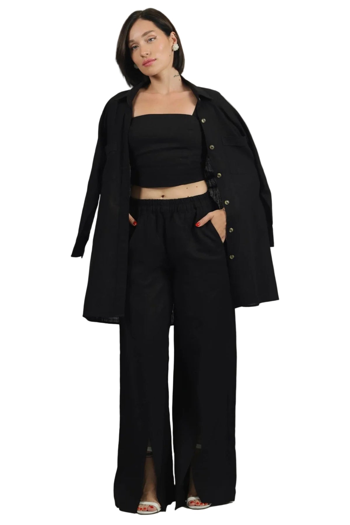 A woman modeling a black coordinated outfit consisting of a wide-leg pants set with front slits, a strapless crop top, and an open longline button-front jacket, photographed against a plain white studio background.