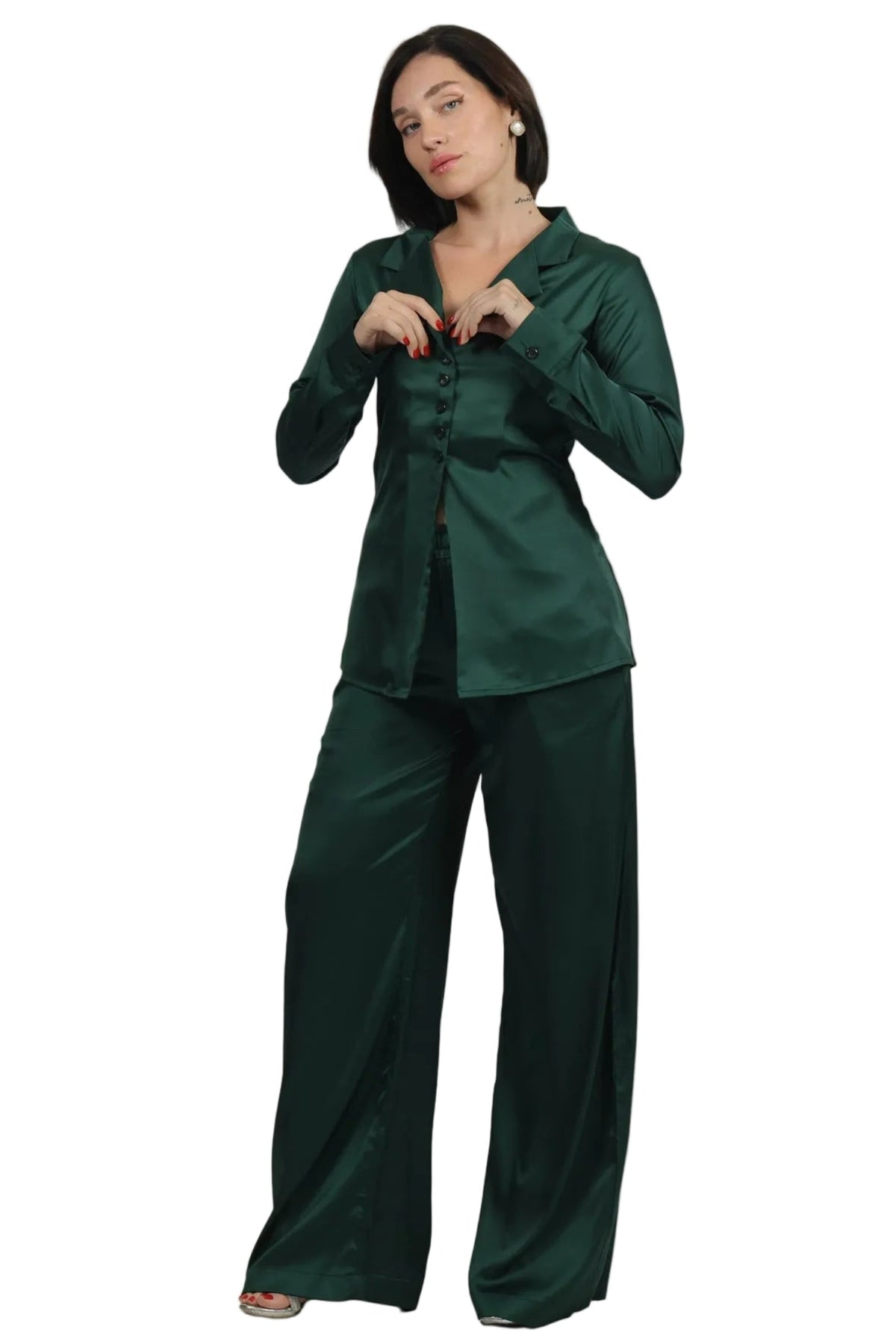 A woman modeling a dark green satin pajama set with a long-sleeve button-up shirt and matching wide-leg pants against a plain white background.