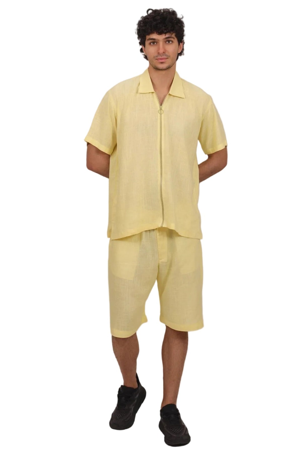 A man modeling a light yellow short-sleeve button-up shirt and matching light yellow shorts against a solid white background.