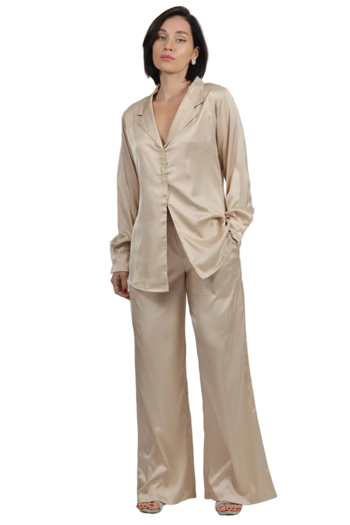 A woman modeling a matching beige satin pajama set with a long-sleeve button-front top and wide-leg pants, photographed against a plain white background.