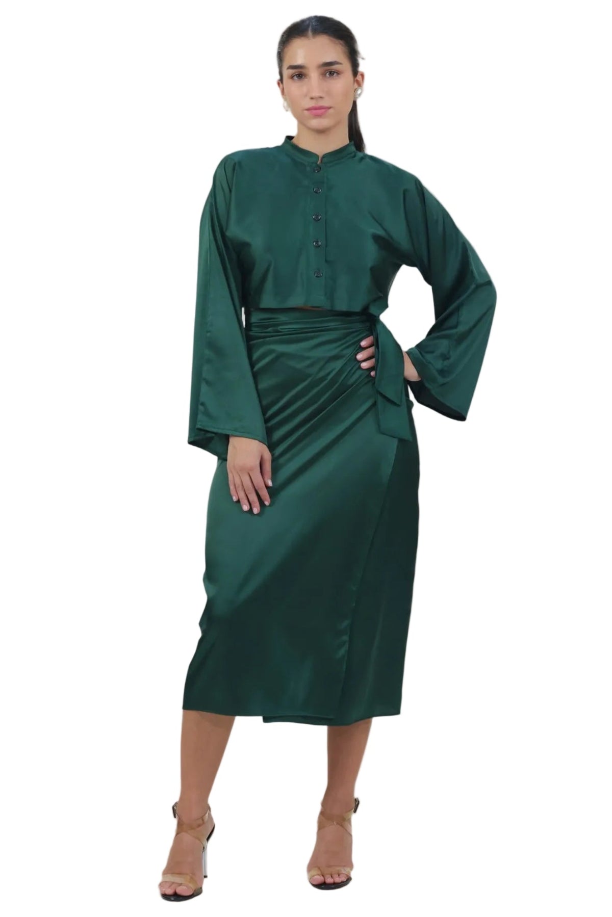 A woman modeling a dark green satin-like long-sleeve dress with a high collar and gathered waist, standing against a plain white background.