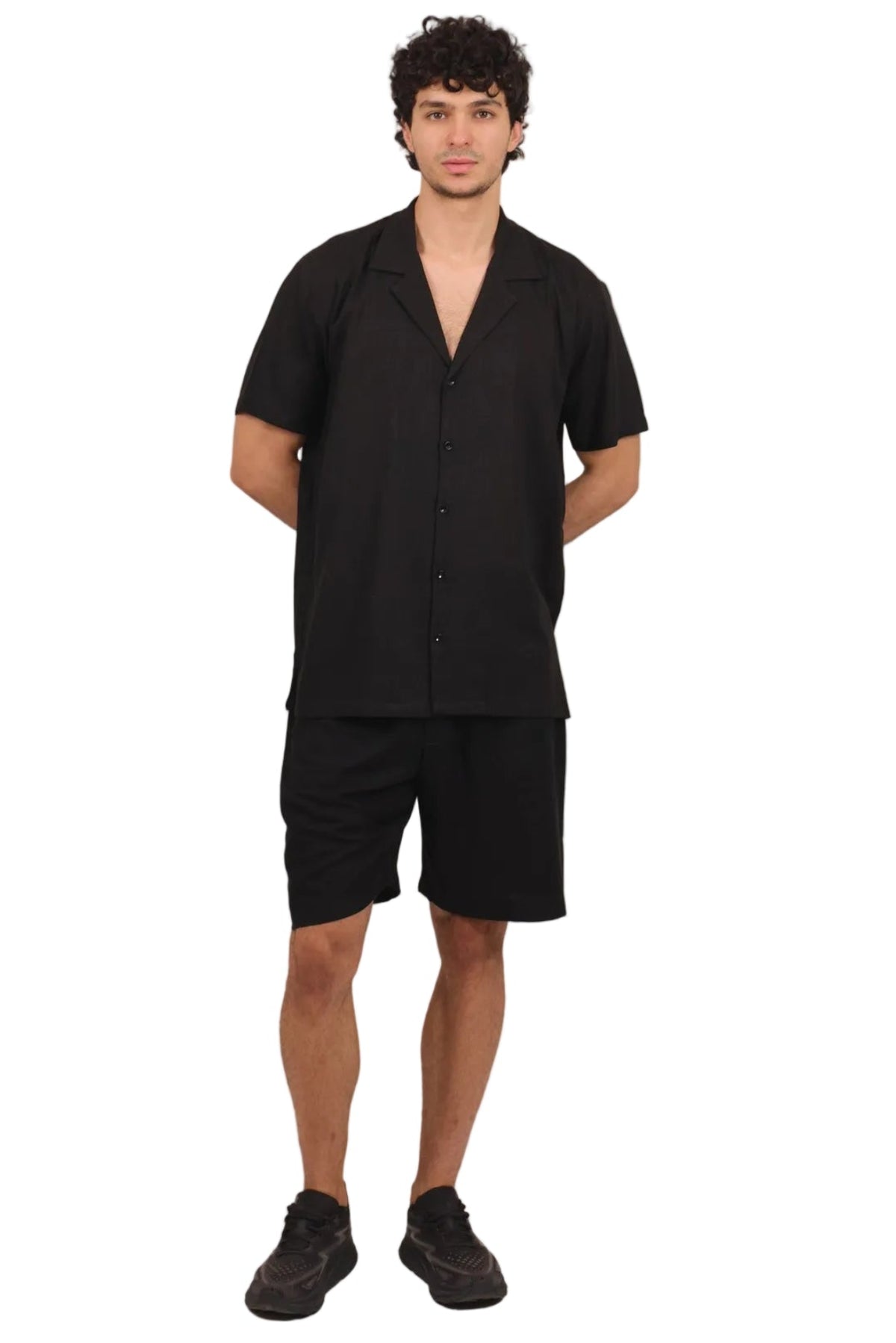 A man modeling a black short-sleeve button-up shirt and matching black shorts against a solid white background.