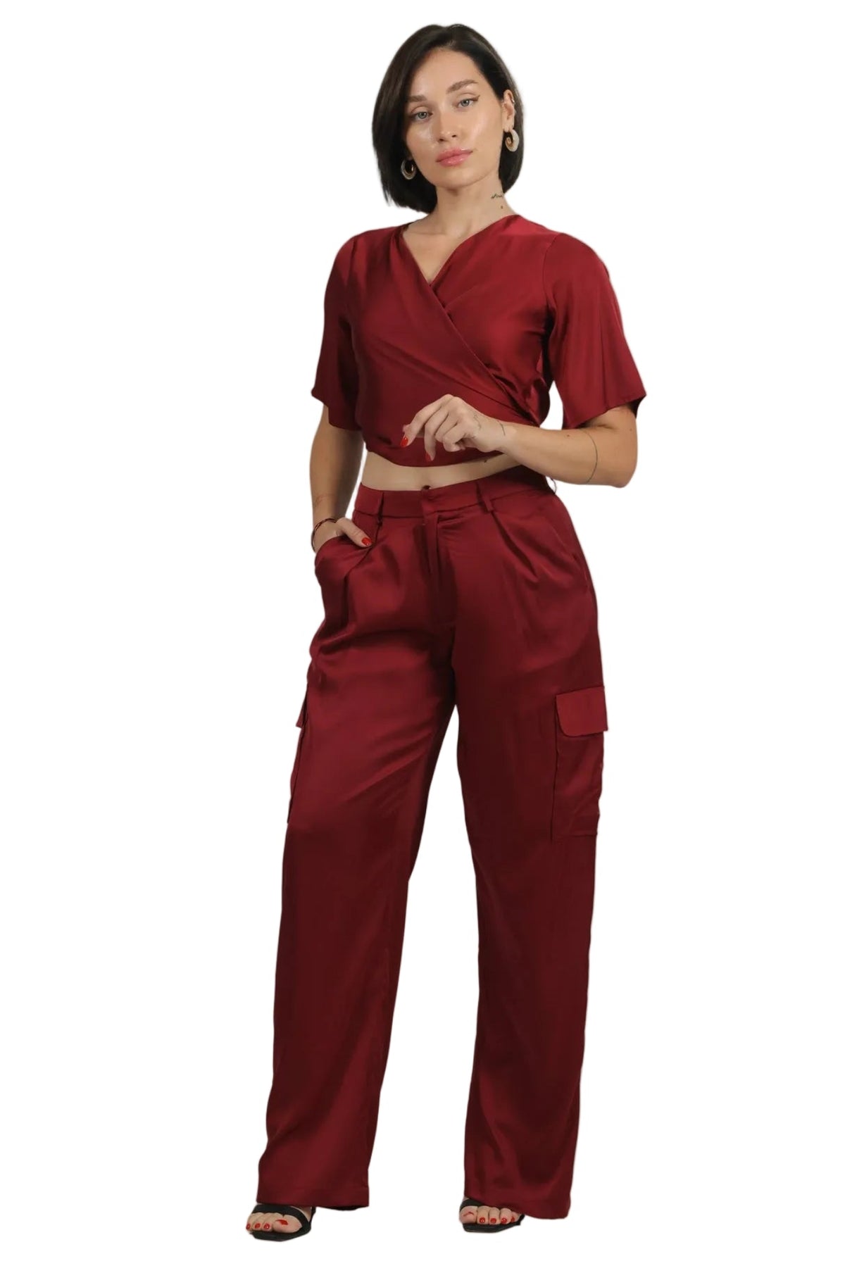A woman modeling a matching two-piece scrub set in deep burgundy, featuring a short-sleeve wrap-style top and high-waisted cargo pants, shot against a solid white background.