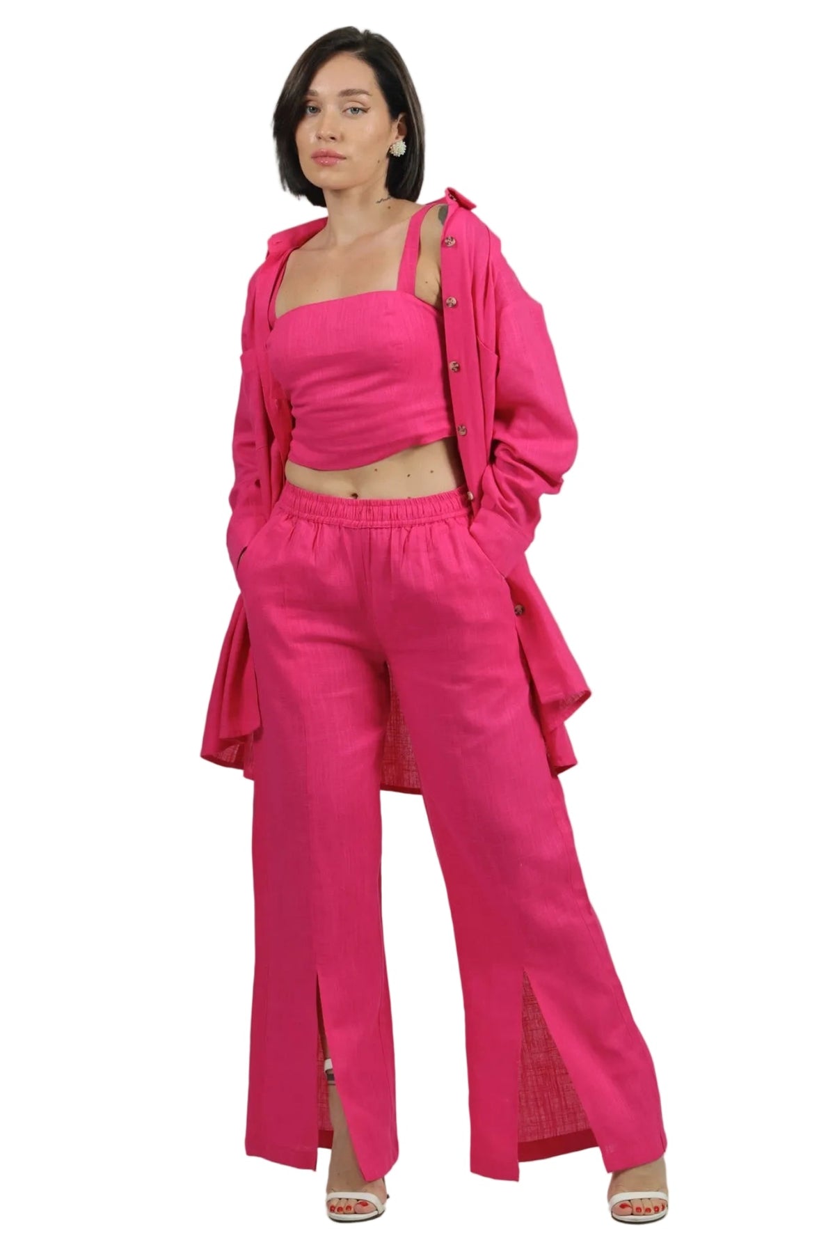 A model wearing a bright pink matching lounge set consisting of a cropped tank top, wide-leg pants with front slits, and an oversized button-up shirt draped off the shoulders, set against a plain white background.