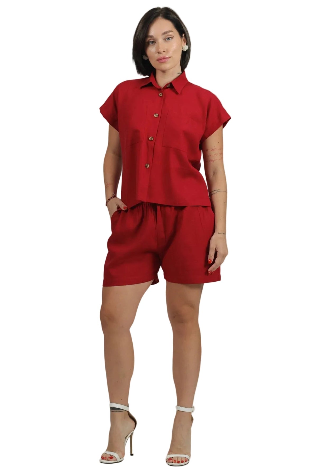 A woman modeling a matching red two-piece set consisting of a short-sleeve button-up shirt and coordinating shorts, paired with white high-heeled sandals, against a plain white background.