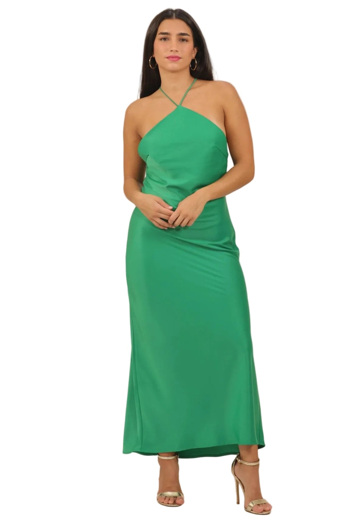 A woman modeling a bright green halter-neck maxi dress with a draped, asymmetrical design, paired with nude high-heeled sandals against a plain white background.