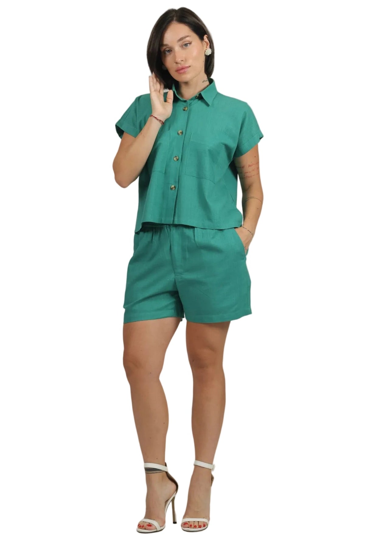 A woman modeling a matching two-piece set consisting of a short-sleeve button-up shirt and coordinating shorts in a vibrant teal green color, styled with white high-heeled sandals against a plain white background.