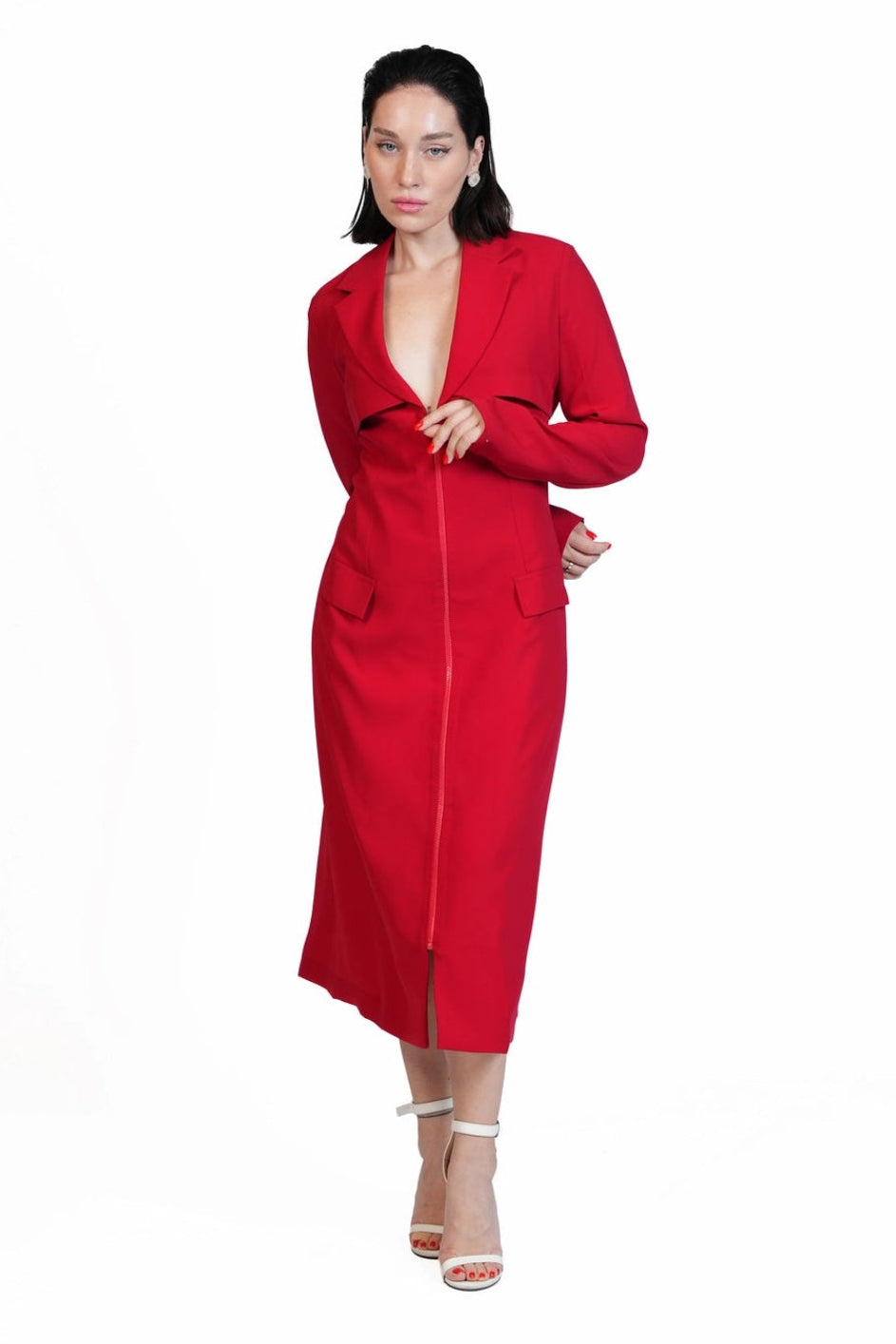 A woman modeling a bright red long-sleeve midi dress with a wrap-style front and side pockets, paired with white heeled sandals, against a plain white background.