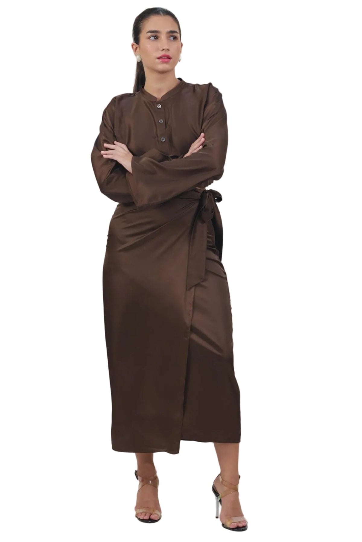 A woman modeling a dark brown long-sleeved maxi dress with a buttoned collar and a matching fabric tie belt, standing against a solid white background.