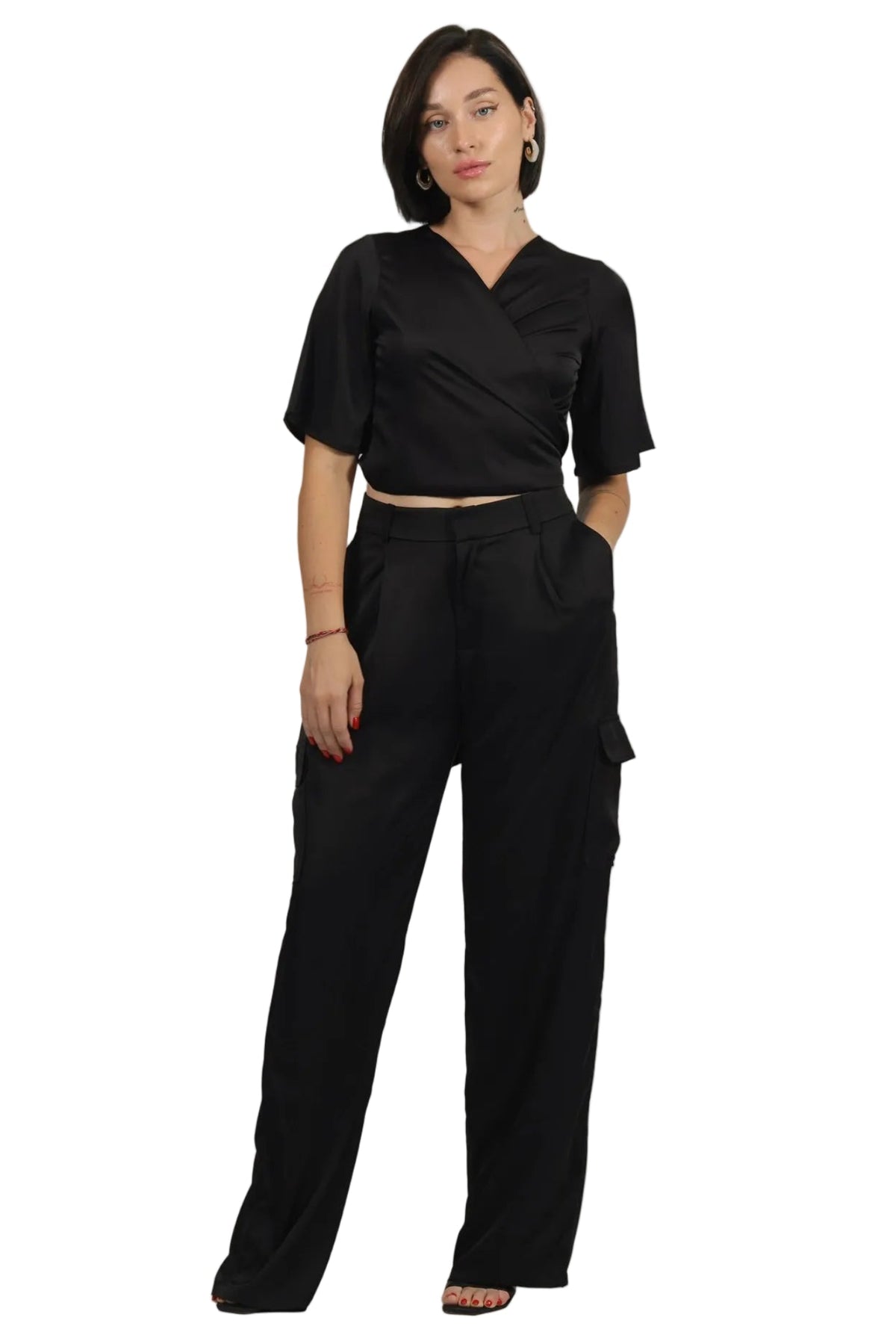 A woman modeling a black two-piece outfit consisting of a short-sleeve wrap-style crop top and matching high-waisted wide-leg cargo pants, shown against a plain white background.
