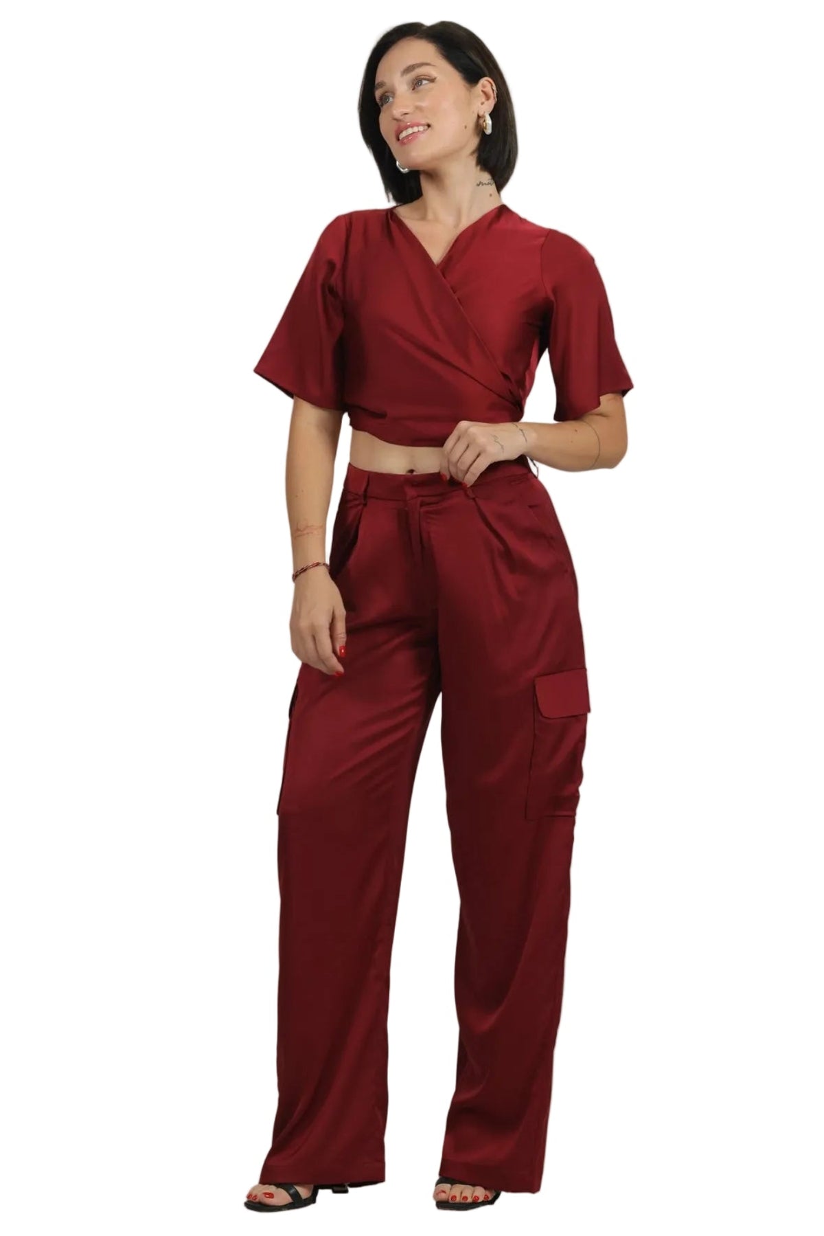 A woman modeling a matching two-piece medical scrub set in a deep red color, featuring a short-sleeve wrap-style top and high-waisted cargo pants, shot against a solid white background.
