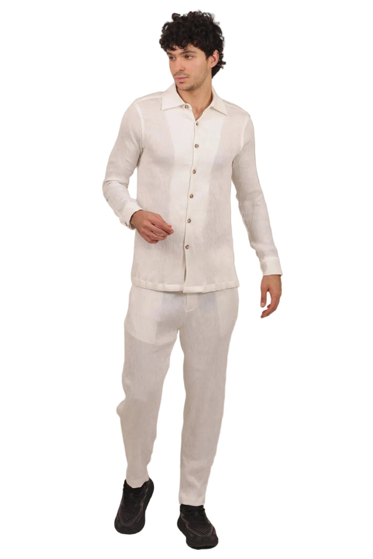 A man modeling a light beige linen two-piece set consisting of a long-sleeve button-up shirt and matching trousers, paired with black shoes, against a solid white background.