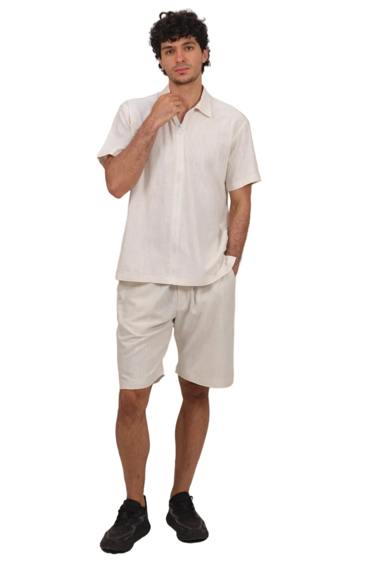 A man modeling a matching light beige short-sleeve button-up shirt and shorts set, paired with black sneakers, against a solid white background.