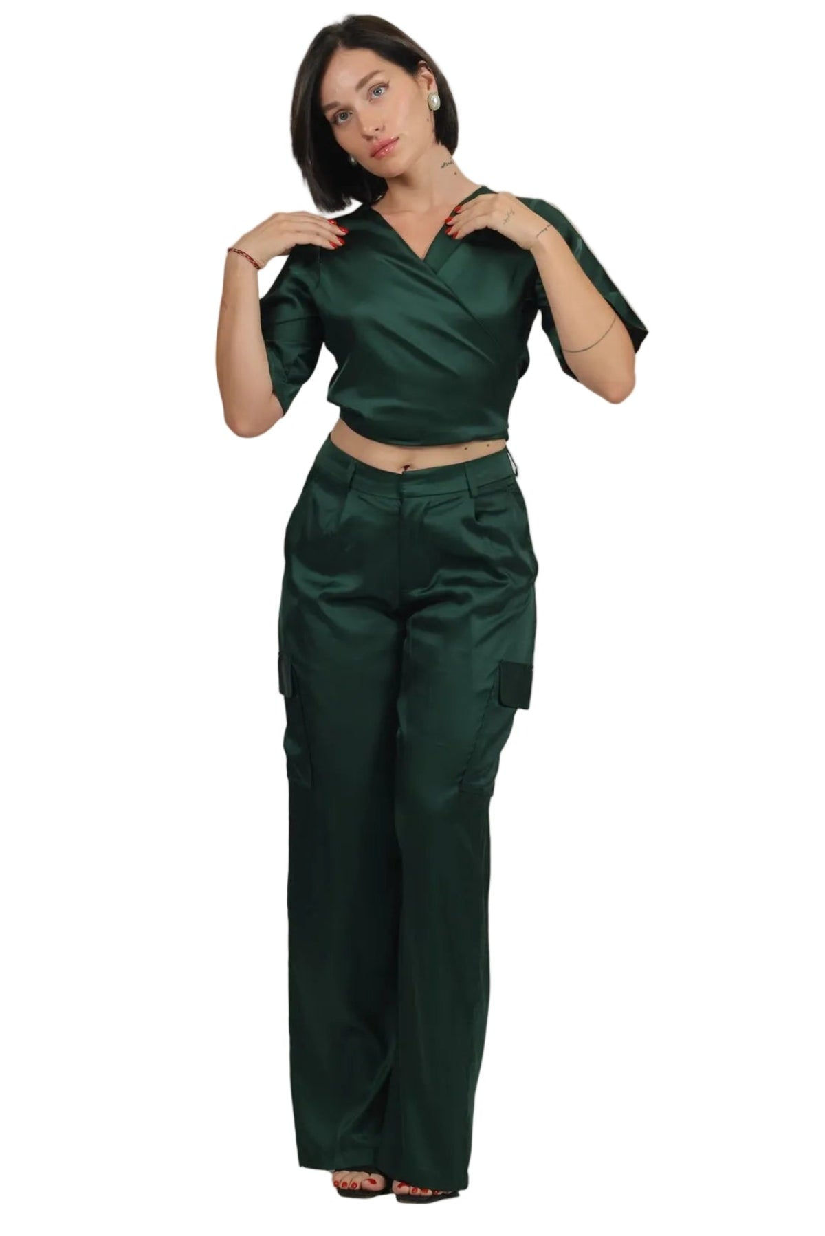 A woman modeling a dark green two-piece set consisting of a short-sleeve wrap-style crop top and matching wide-leg trousers, shown against a plain white background.