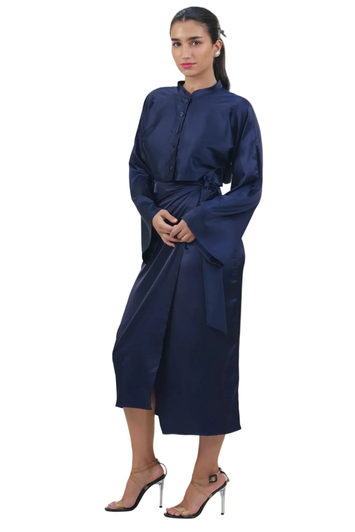 A woman modeling a dark navy blue long-sleeved dress with a high collar and a matching waist tie, paired with clear high-heeled sandals, set against a plain white background.