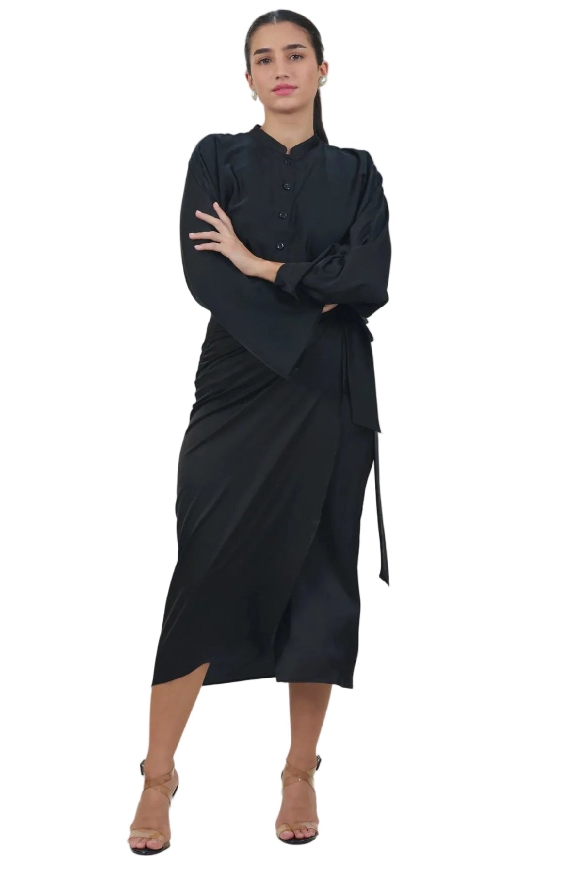 A woman modeling a black long-sleeve wrap-style dress with a high collar and side tie, standing against a plain white background.