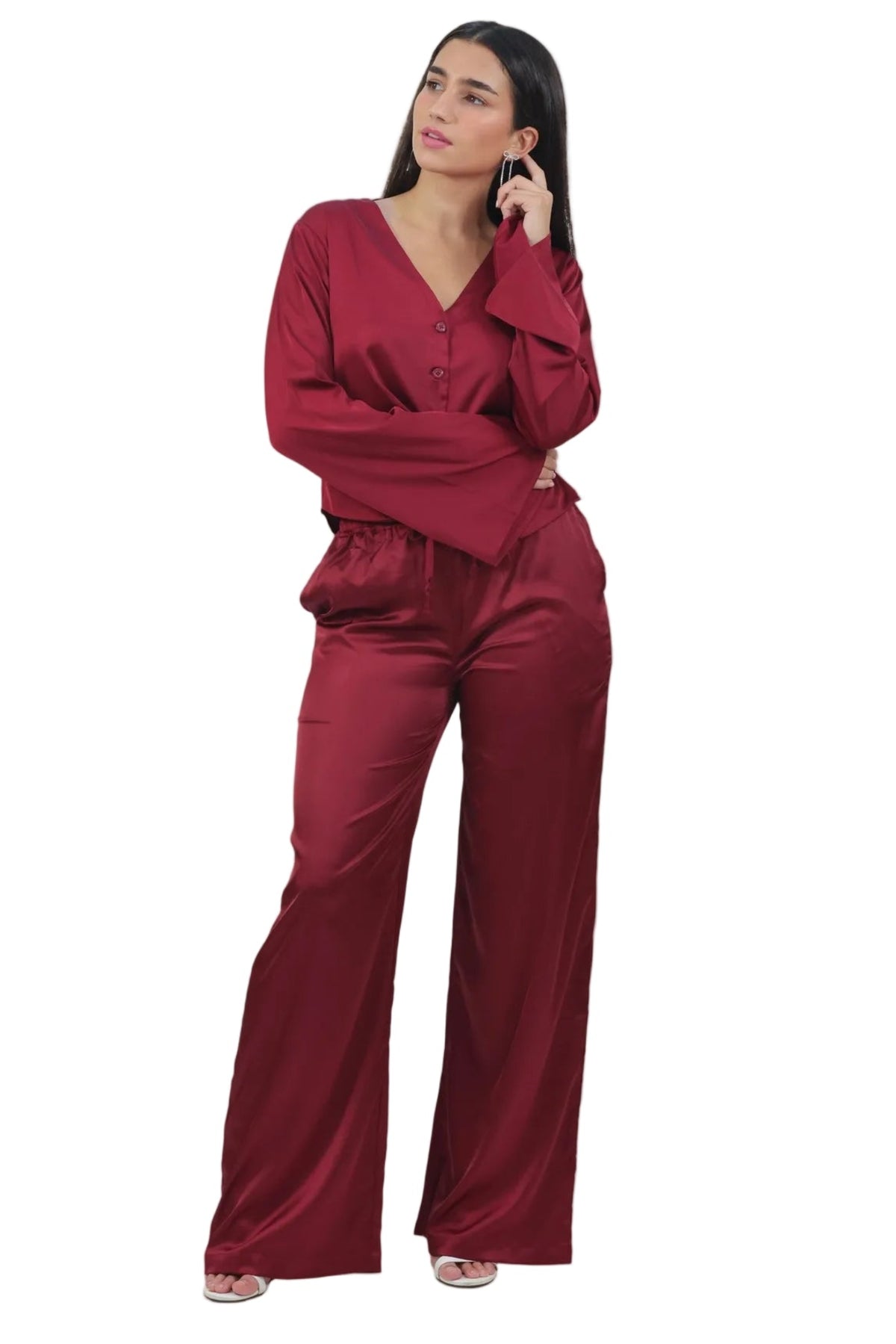 A woman modeling a matching burgundy satin two-piece set consisting of a long-sleeve V-neck top and wide-leg pants, set against a plain white background.