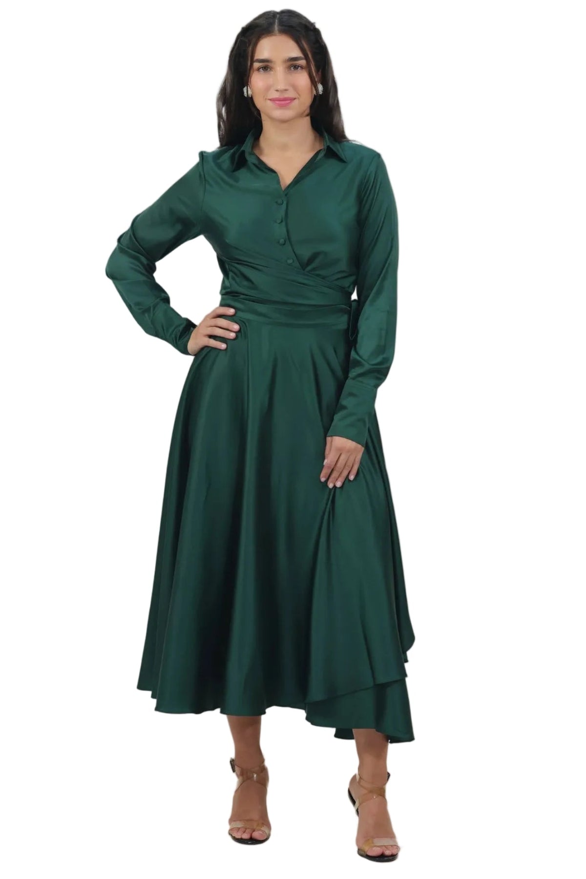 A woman modeling a dark green long-sleeve midi dress with a wrap-style bodice and flared skirt, paired with tan heeled sandals, against a plain white background.
