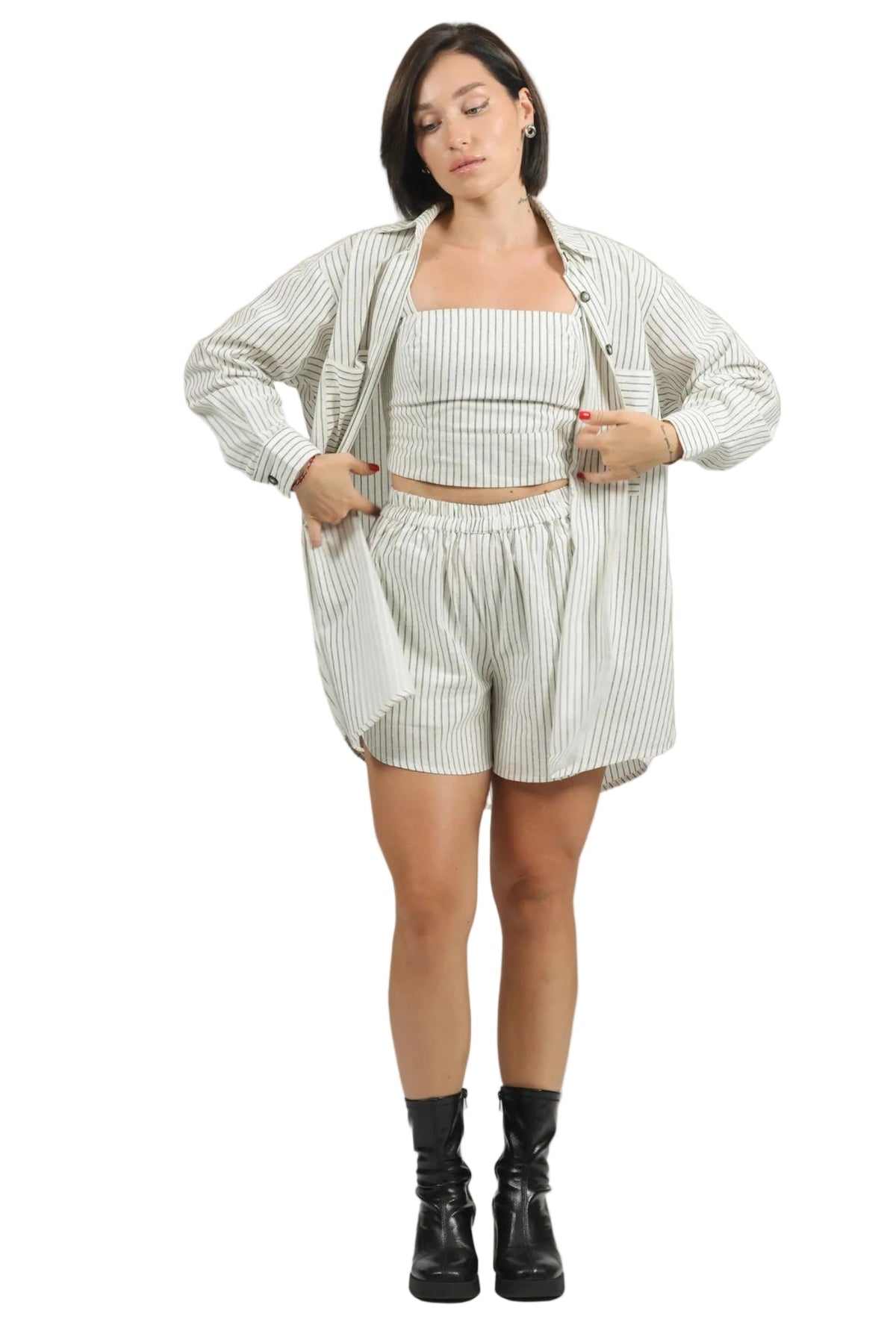 A woman modeling a matching striped lounge set consisting of a cropped tank top, shorts, and an open-front overshirt, paired with black ankle boots, against a solid white background.