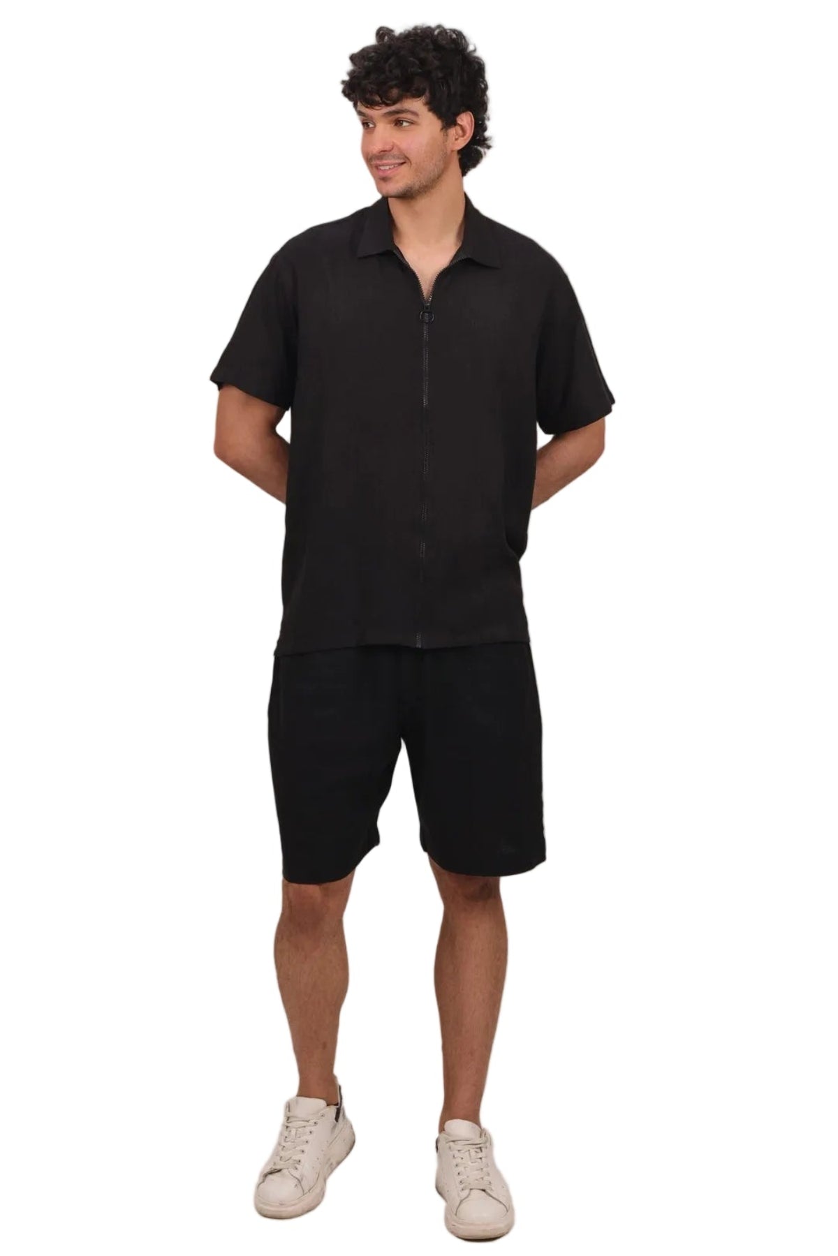 A man modeling a black short-sleeve polo shirt with a half-zip front and black shorts, paired with white sneakers, against a solid white background.
