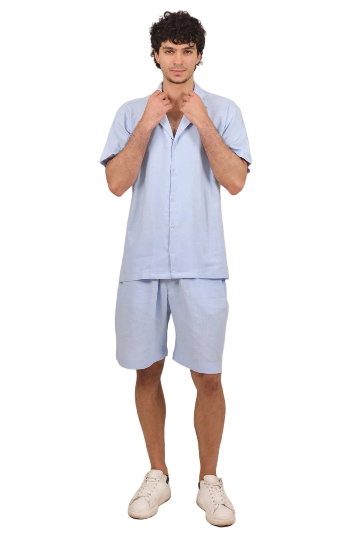 A man modeling a light blue short-sleeve button-up shirt and matching shorts set, paired with white sneakers, against a solid white background.