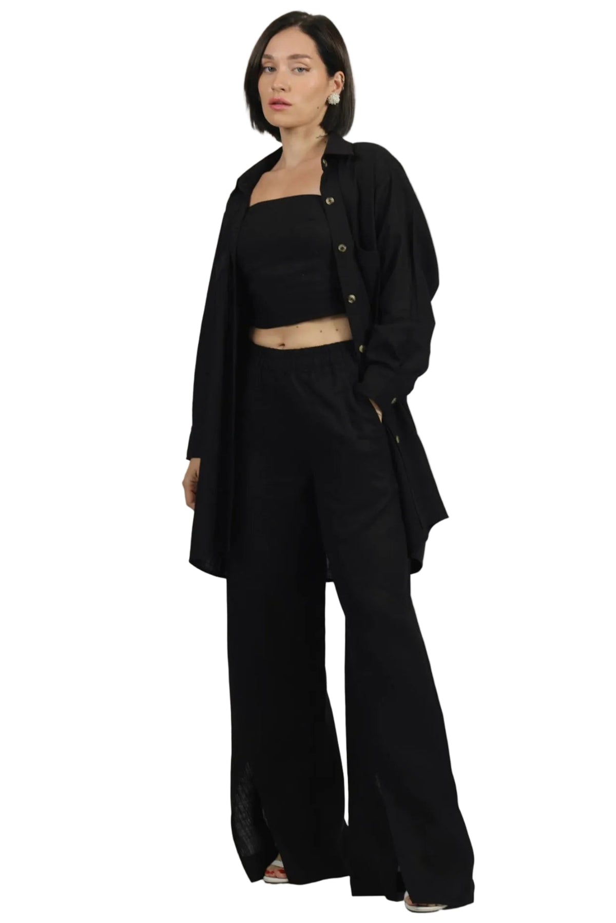 A model wearing a black streetwear outfit consisting of a long-sleeve button-up shirt, a black crop top, and wide-leg black pants, photographed against a solid white background.