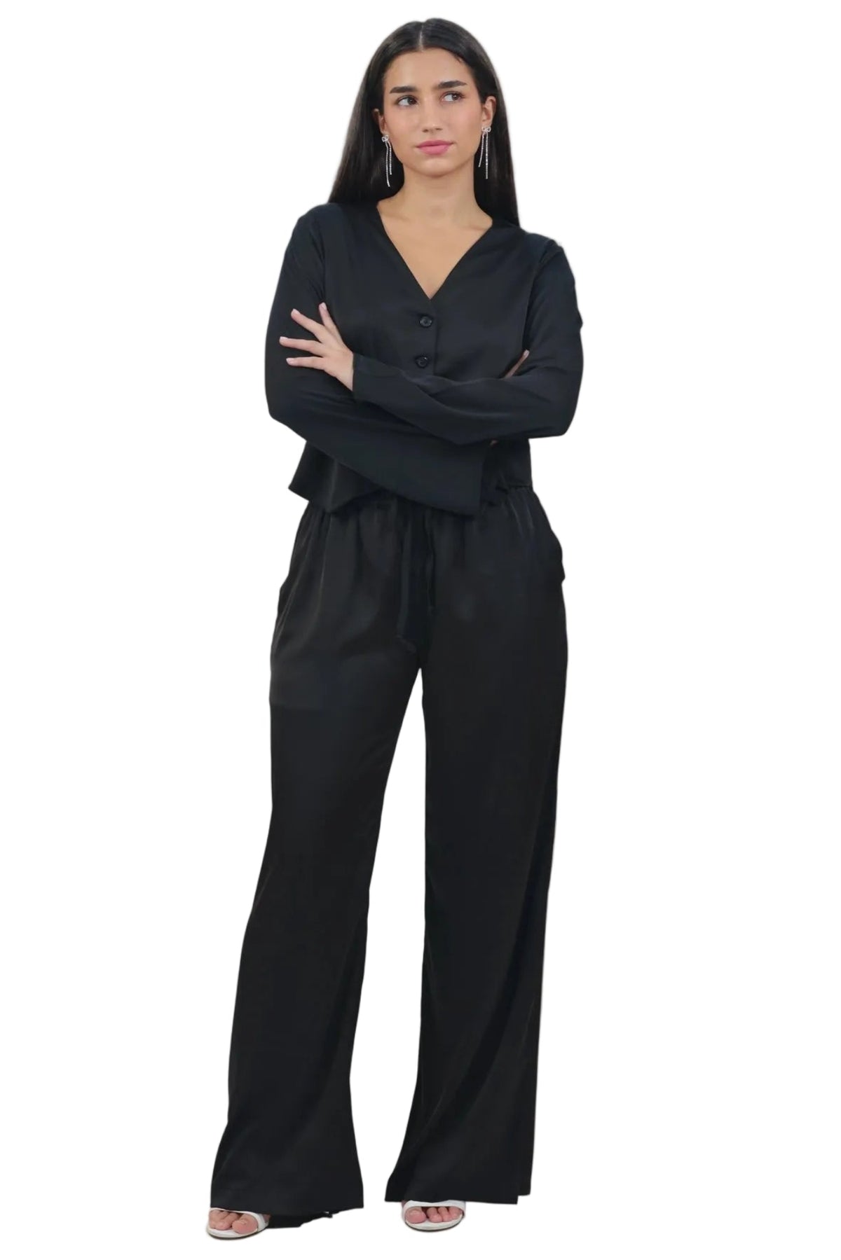 A woman modeling a black long-sleeve jumpsuit with a V-neckline and wide-leg pants, standing against a solid white background.