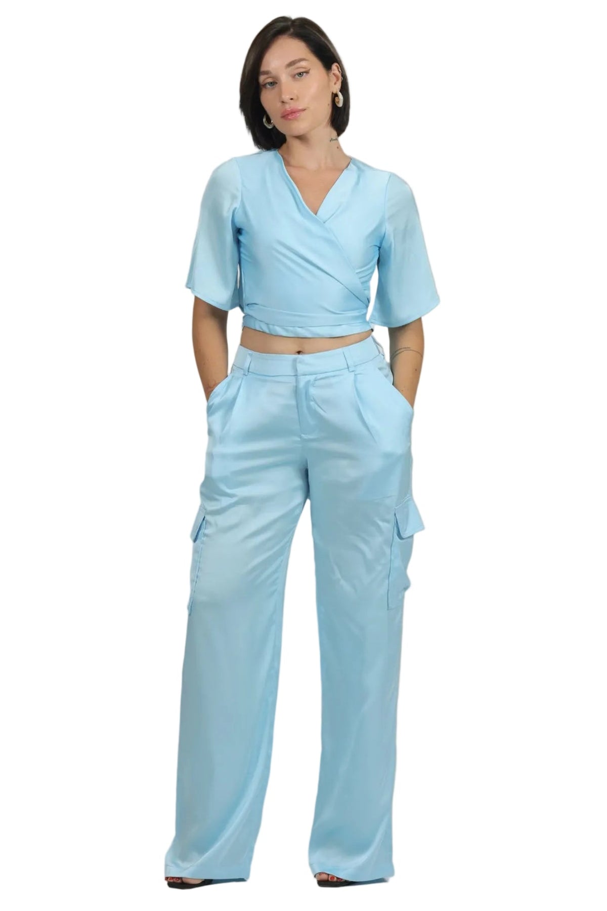 A woman modeling a light blue set consisting of a short-sleeve wrap-style top and matching cargo pants, photographed against a solid white background.