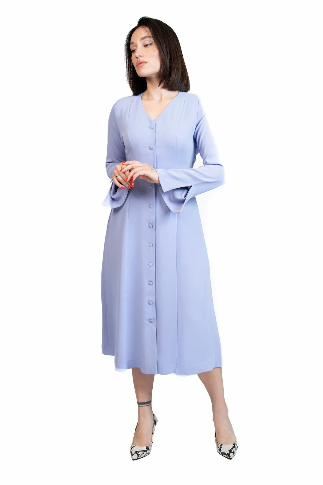 A woman modeling a light blue long-sleeve midi dress with a button-down front and flared cuffs, paired with silver heels, against a plain white background.