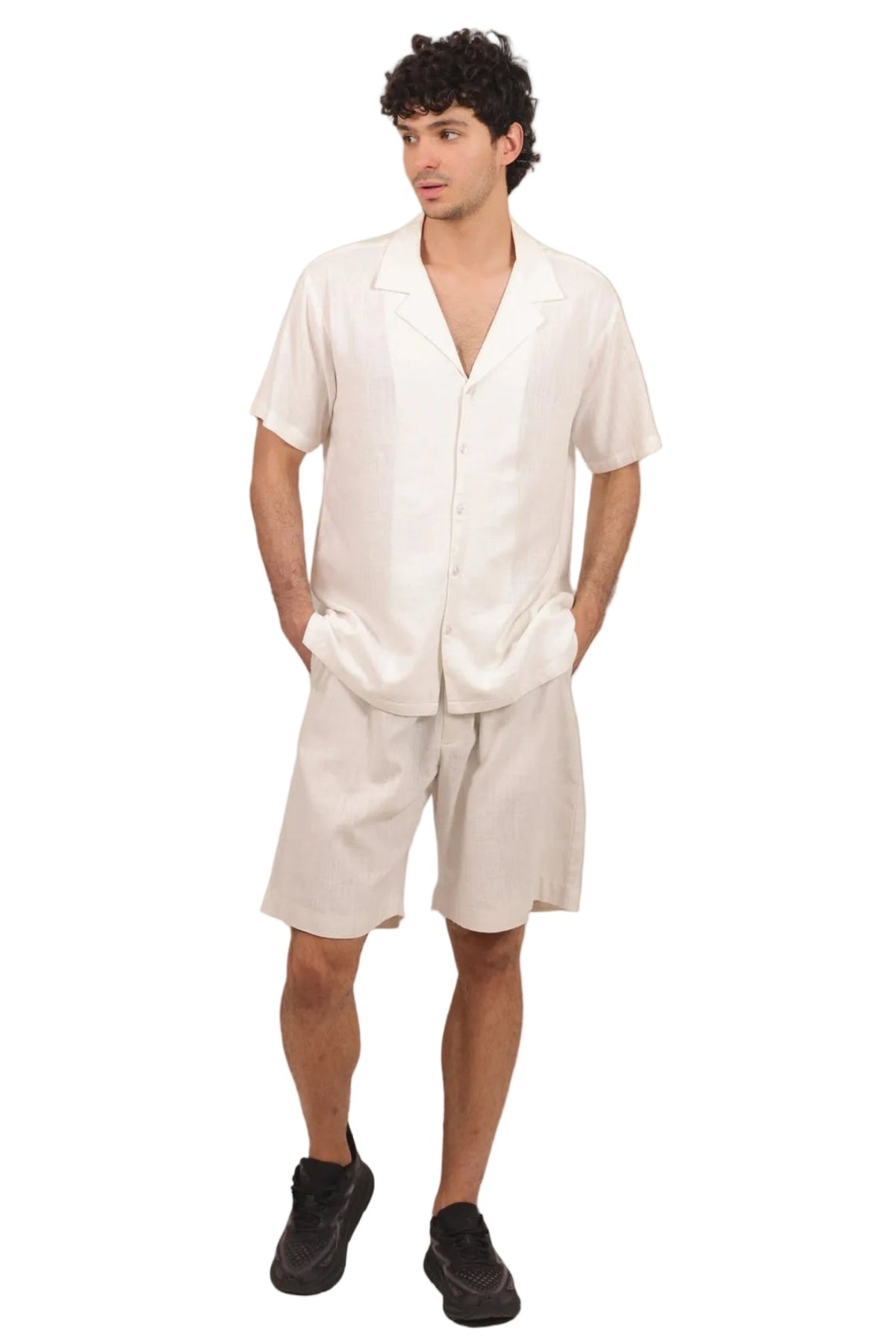 A man modeling a matching off-white linen short-sleeve button-up shirt and shorts set, paired with black sneakers, against a solid white background.