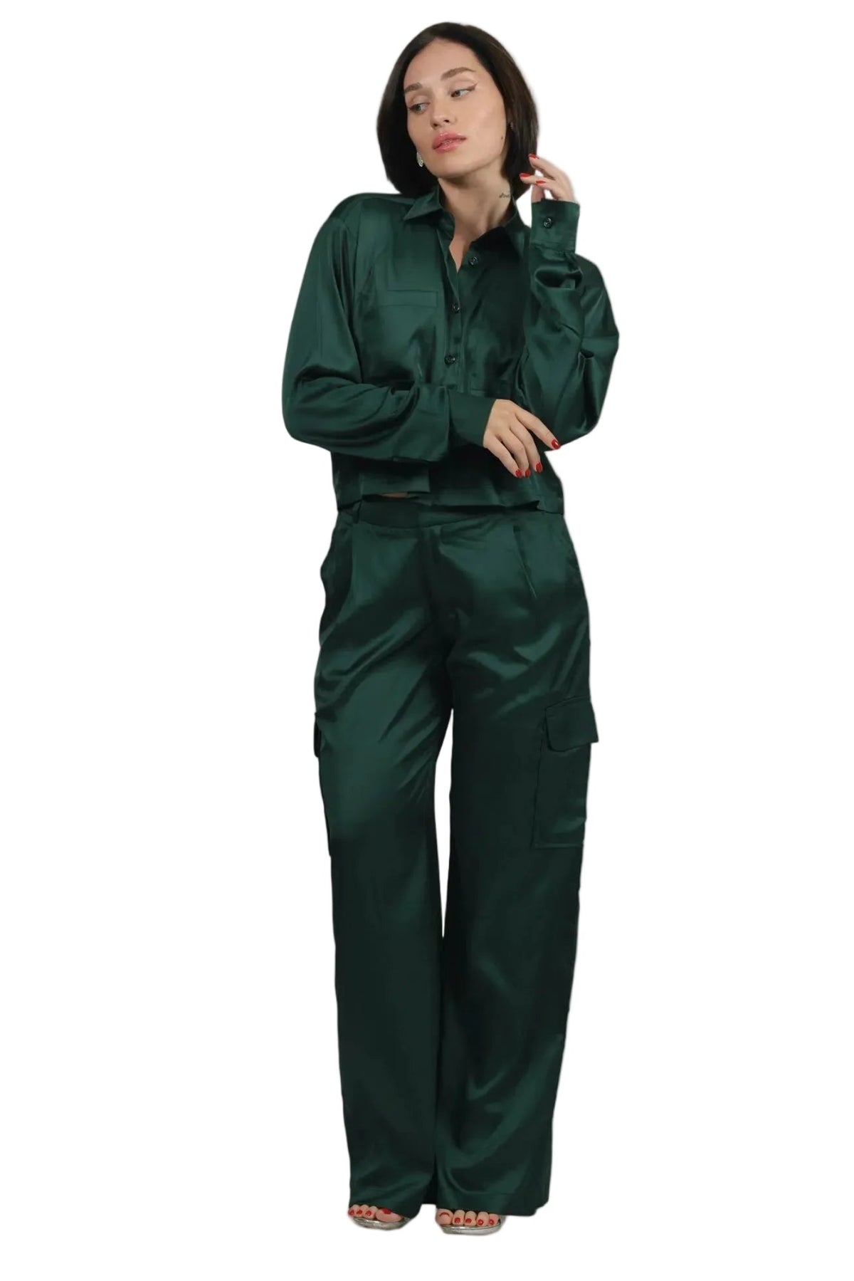 A woman modeling a dark green satin two-piece set consisting of a long-sleeve button-up shirt and matching wide-leg cargo pants, set against a solid beige background.