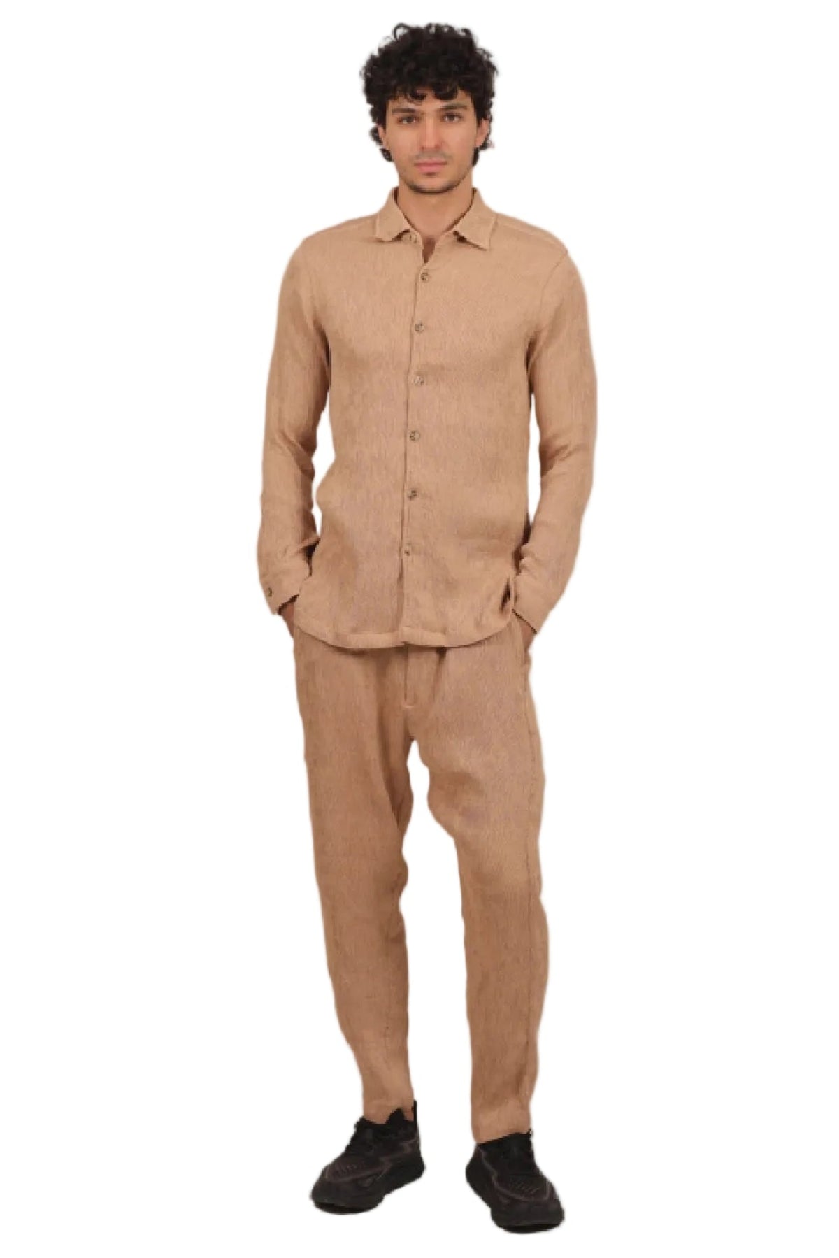 Man wearing a beige shirt and pants standing against a beige background