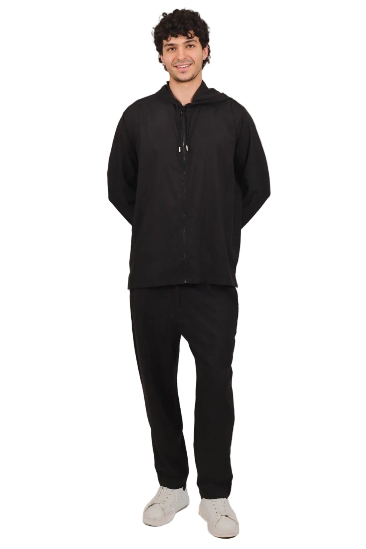 A man wearing a black zip-up hoodie and matching black sweatpants, standing against a solid white background.