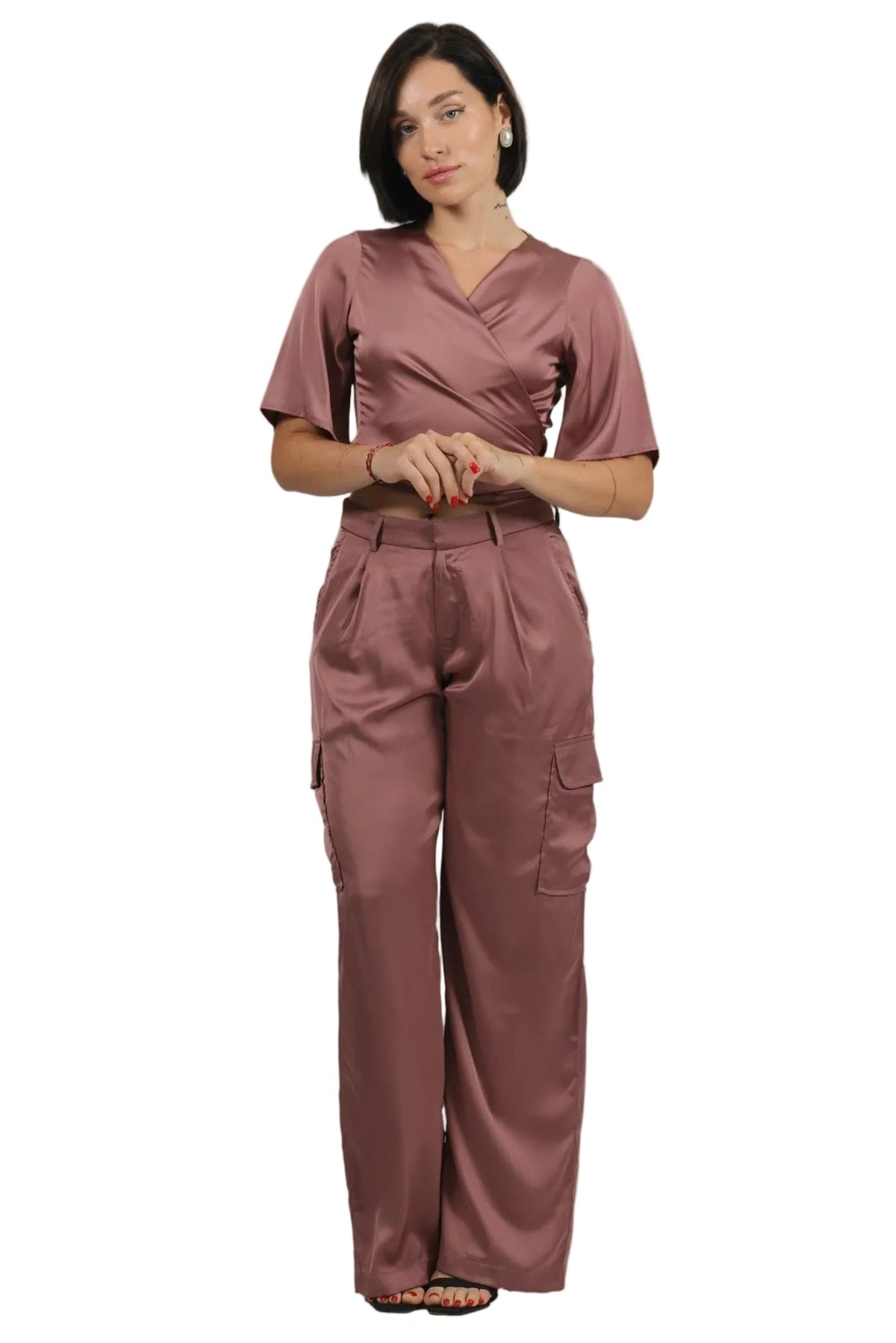 A woman modeling a matching two-piece medical scrub set in a dusty rose color, featuring a short-sleeve wrap-style top and high-waisted cargo pants, shot against a plain white background.