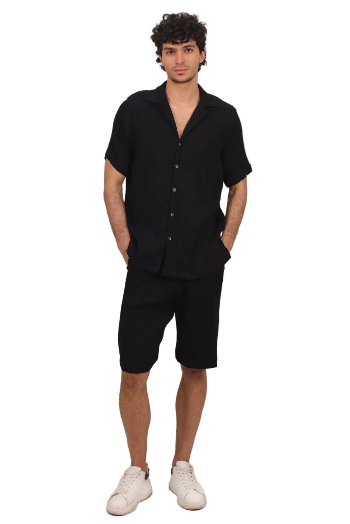 A man modeling a black short-sleeve button-up shirt and matching black shorts, paired with white sneakers, against a solid white background.