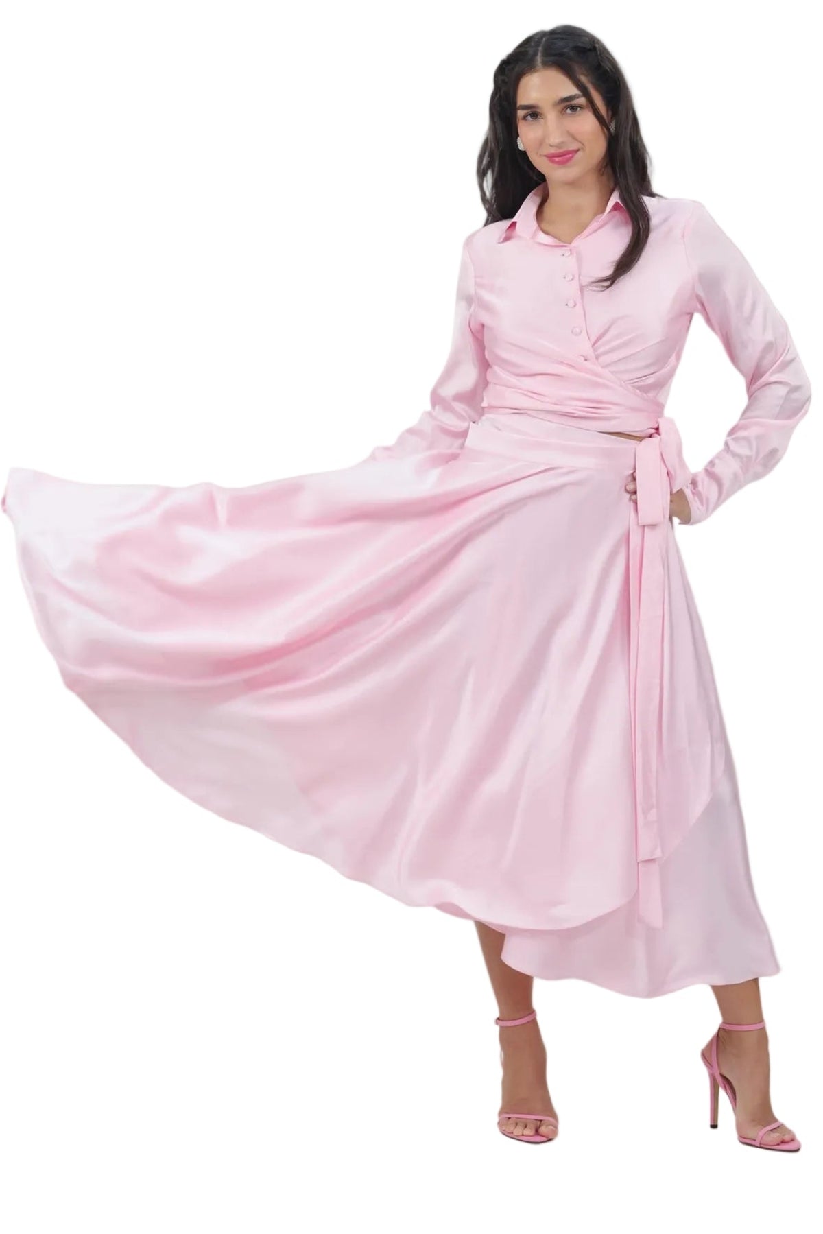 A woman modeling a light pink long-sleeve midi dress with a wrap-style waist and matching tie belt, posed against a solid white background.