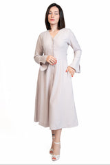 A woman modeling a light beige long-sleeve midi dress with a V-neckline and buttoned front, standing against a plain white background.