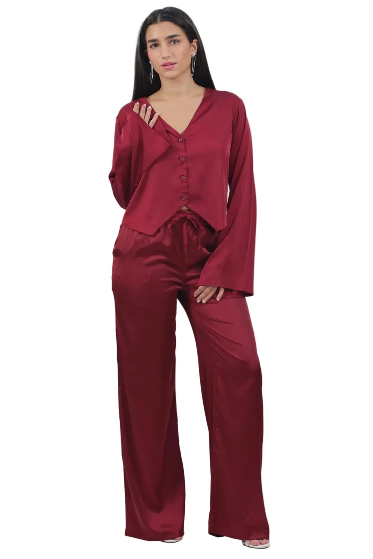 A woman modeling a matching burgundy satin pajama set with a long-sleeve button-front top and wide-leg pants, photographed against a plain white background.