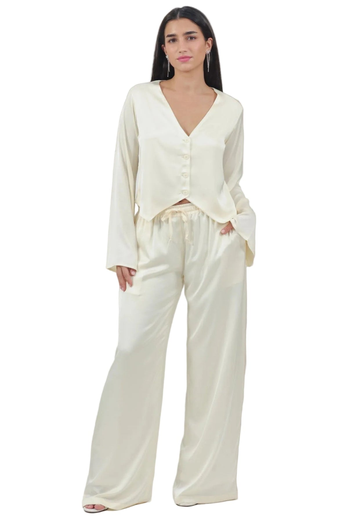 A woman modeling a cream-colored two-piece lounge set consisting of a long-sleeve button-front top and matching wide-leg pants, set against a plain white background.