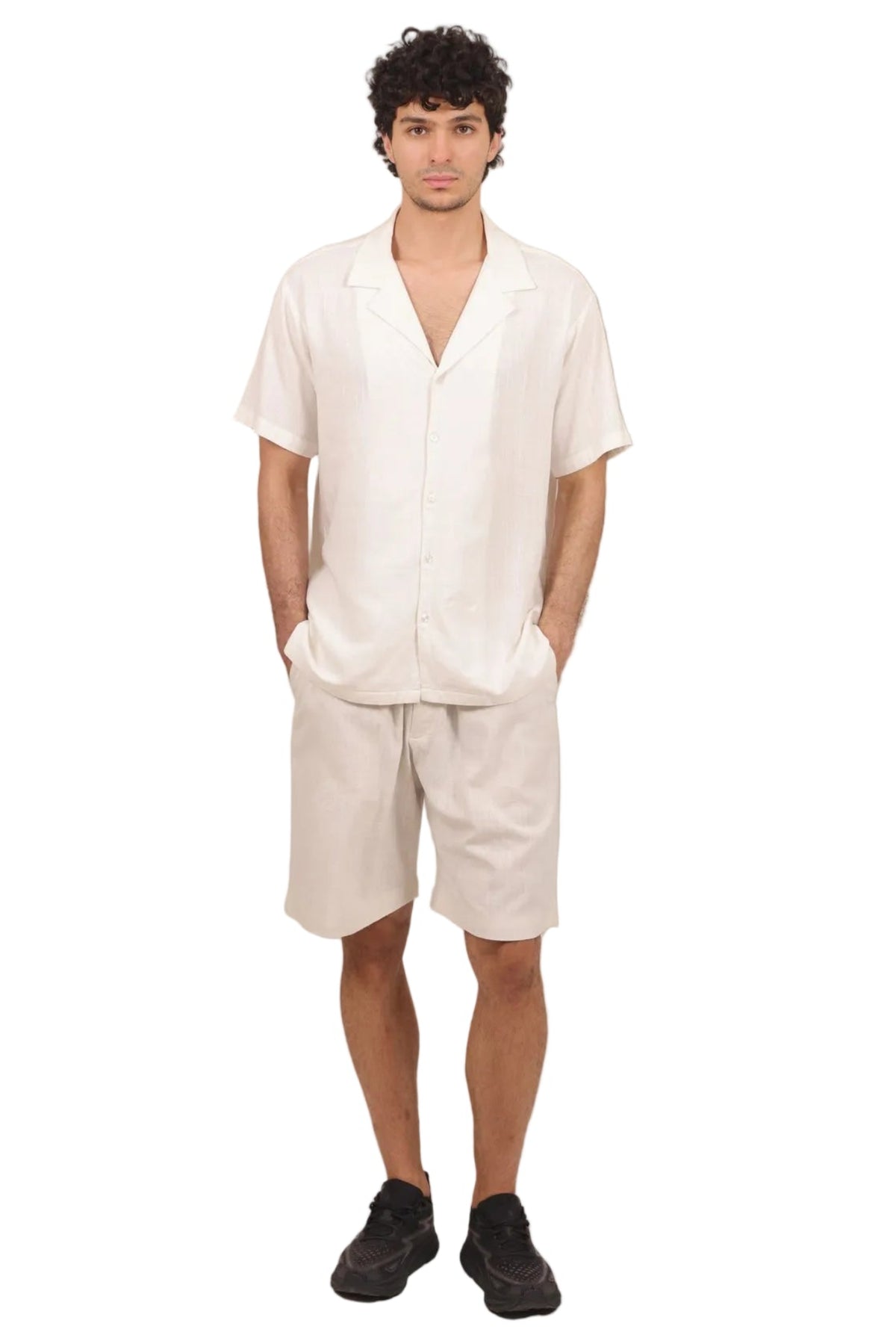 A man modeling a matching off-white linen short-sleeve button-up shirt and shorts set, paired with black sneakers, against a solid white background.