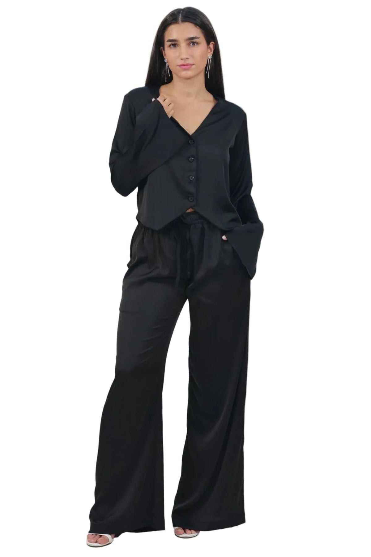 A woman modeling a black two-piece outfit consisting of a long-sleeve wrap-style top with button details and matching wide-leg pants, photographed against a solid white background.