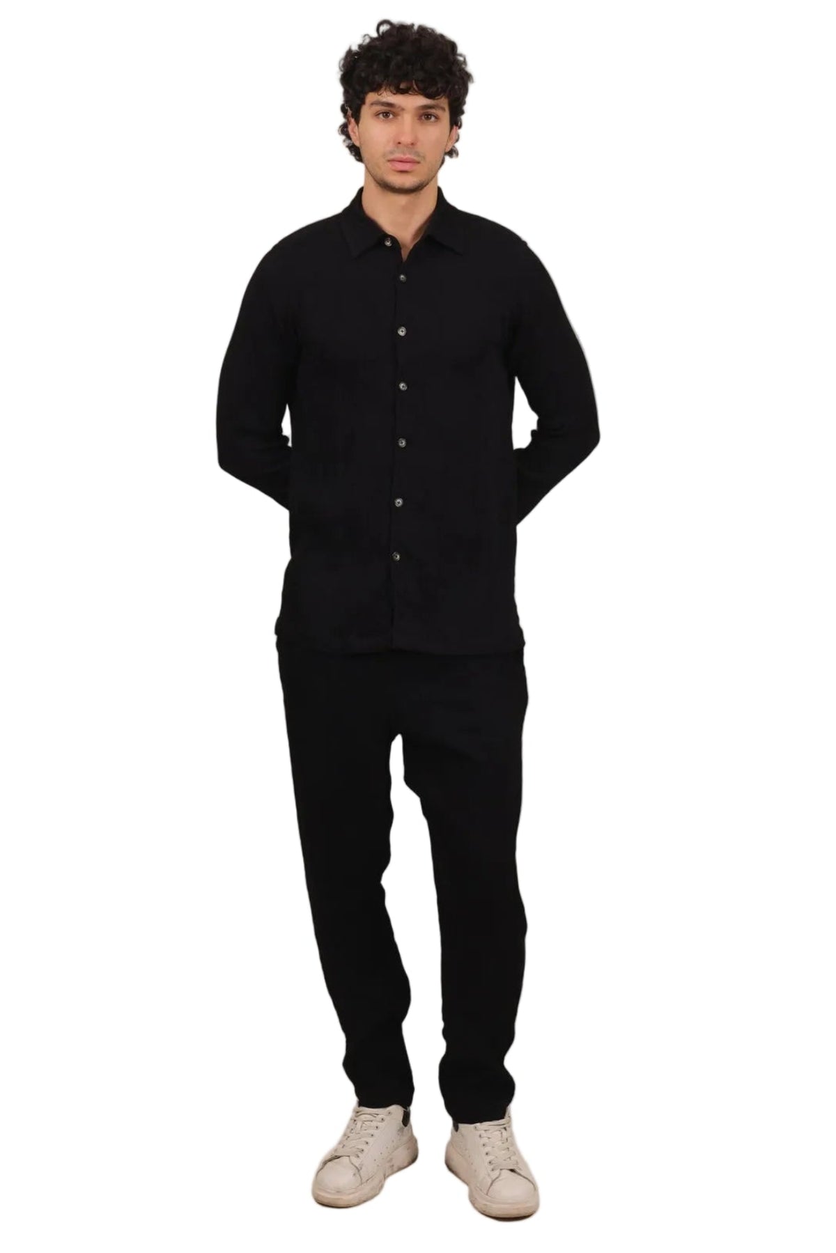 A man modeling a black long-sleeve button-up shirt and black pants with off-white sneakers, standing against a solid white background.